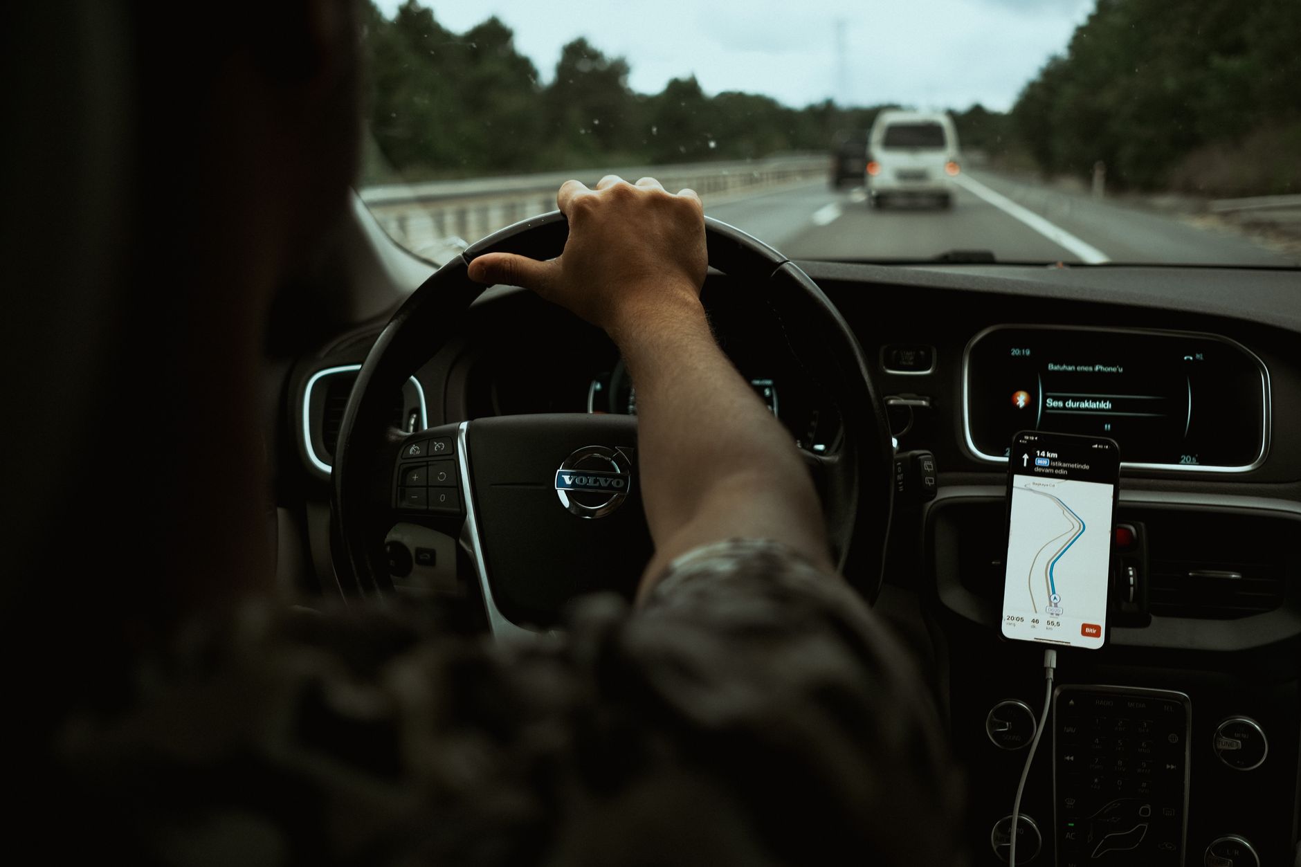 Blick vom Rücksitz über die Schulter des Fahrers auf Lenkrad und ein Smartphone mit Navigations-App am Armaturenbrett